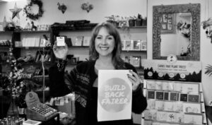 A woman in a Fair Trade gift shop holding a Build Back Fairer sign and a Fair Trade necklace